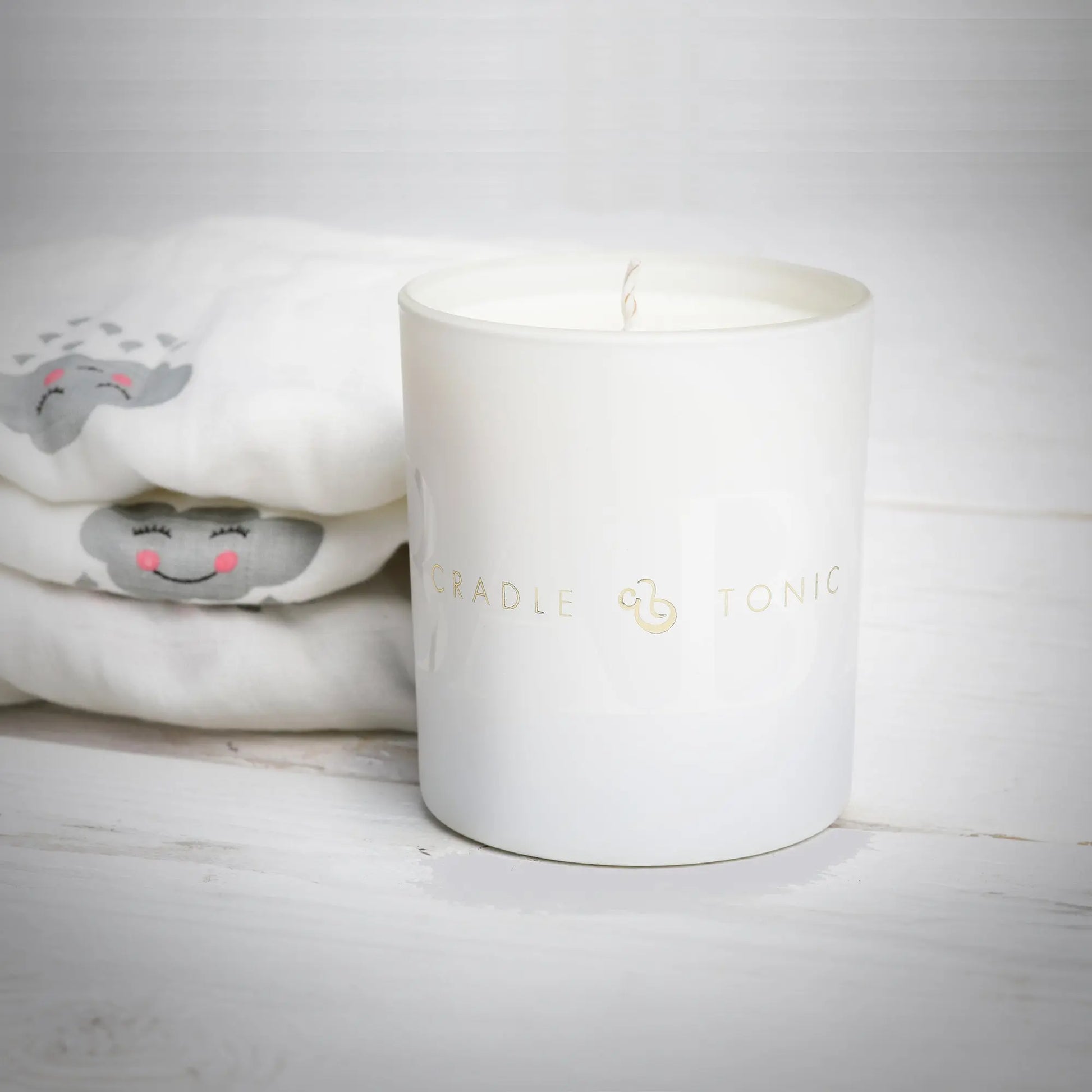 Mum and Baby Candle by Cradle & Tonic placed beside baby clothes, perfect for creating soothing moments for new mums and babies.