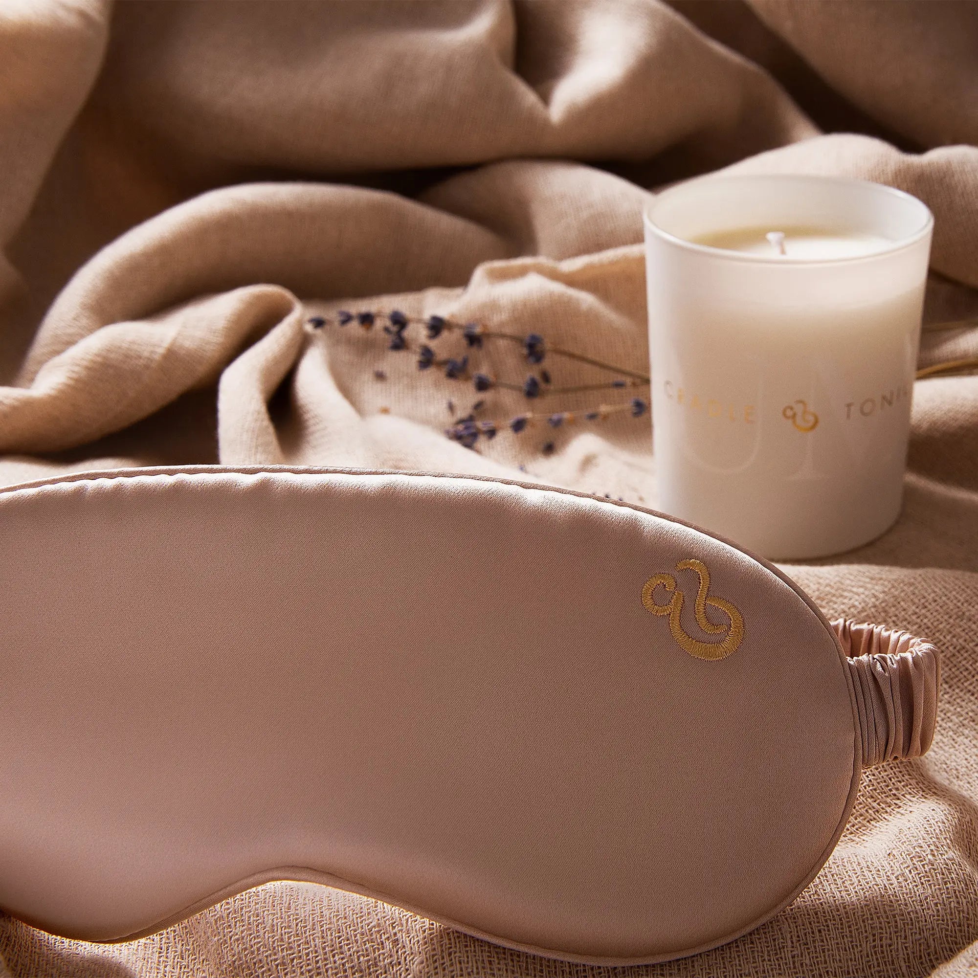 Luxury Sleep Mask - Cradle & Tonic made from 100% mulberry silk in blush pink, shown with branded candle and soft fabric backdrop.